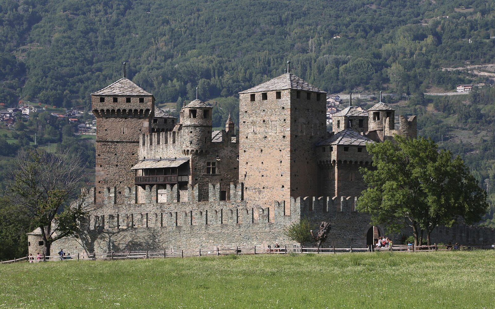Il castello di Fénis con le torri merlate e la doppia cinta di mura, circondato da un prato verde