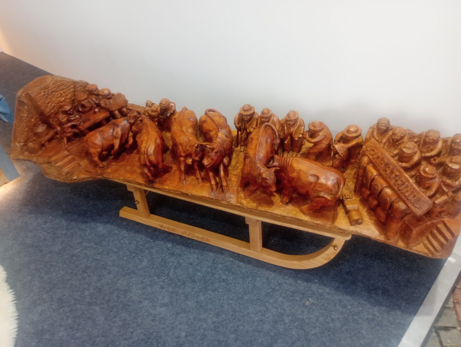 Scultura artigianale in legno su slitta che raffigura bovine e spettatori, esposta alla Fiera di Sant'Orso di Aosta